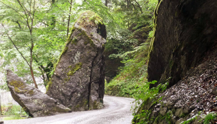Waldweg zwischen zwei grossen Steinen die wie Wächter wirken
