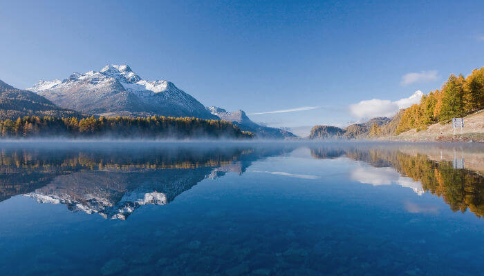 Silsersee mit spiegelnden Bergen und Lärchen im Herbst