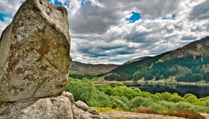 Grosser Stein in grüner Landschaft vor einem See