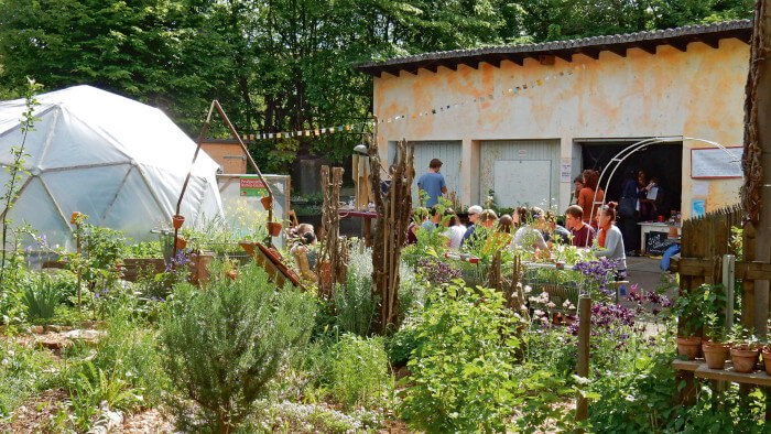 Personengruppe sitzen am Tisch in einem Gemüsegarten vor Hauswand