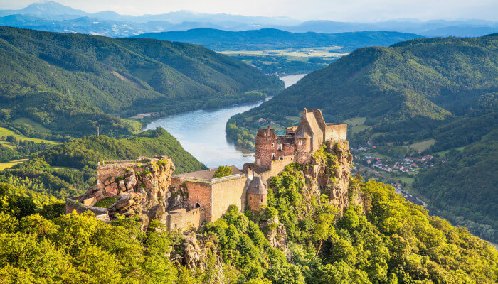 Burg auf einem grünen Hügel vor Fluss in Berglandschaft